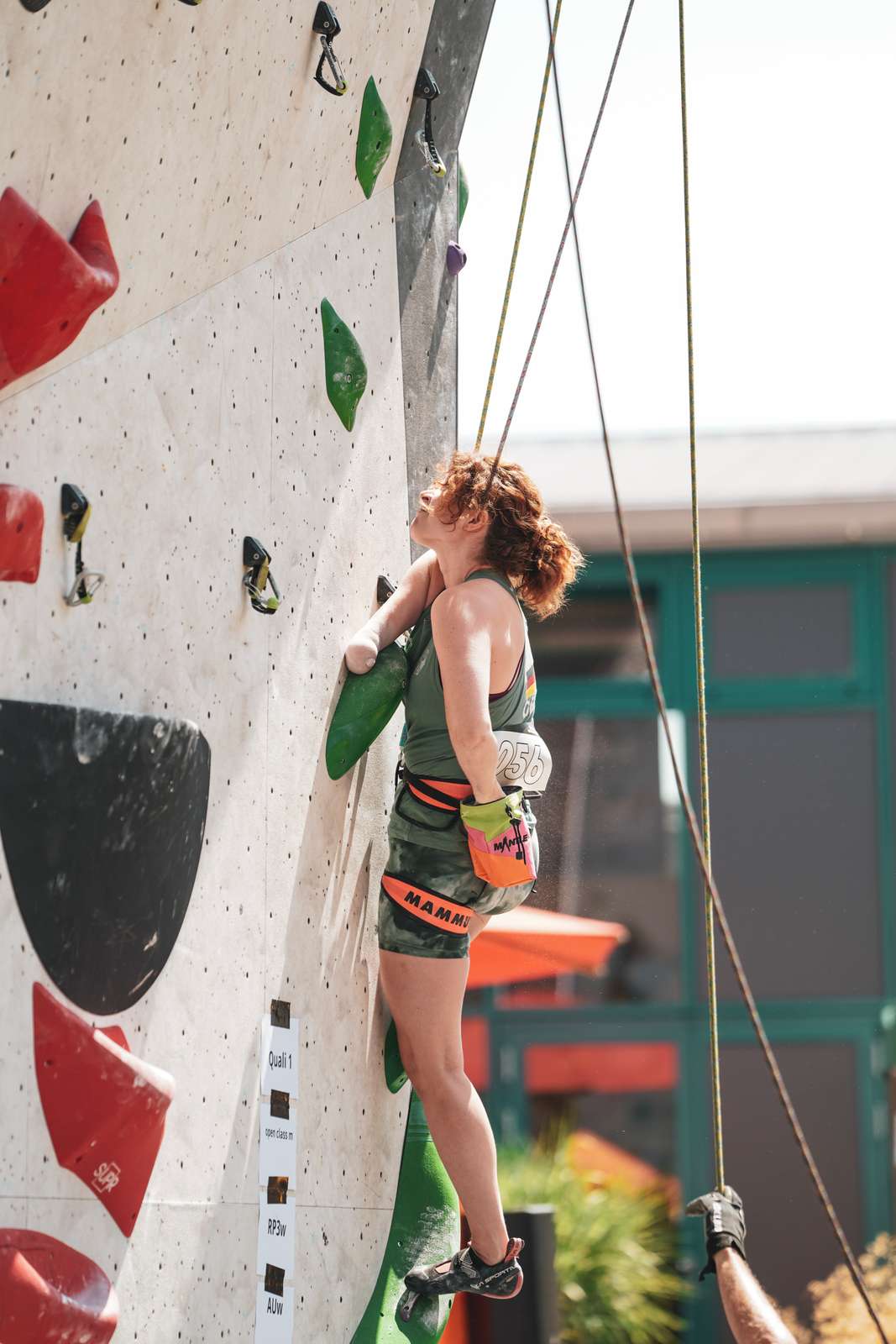 Eine deutsche Para-Athletin inmitten einer Route, die ihren Unterarm hinter einen Griff klemmt, und mit der anderen Hand chalkt